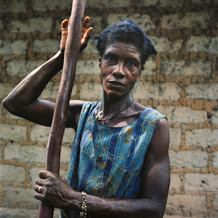Opens popup gallery with A woman takes a break from pounding palm kernels and making palm oil to pose for a portrait. Masethele, Bombali District, Sierra Leone.